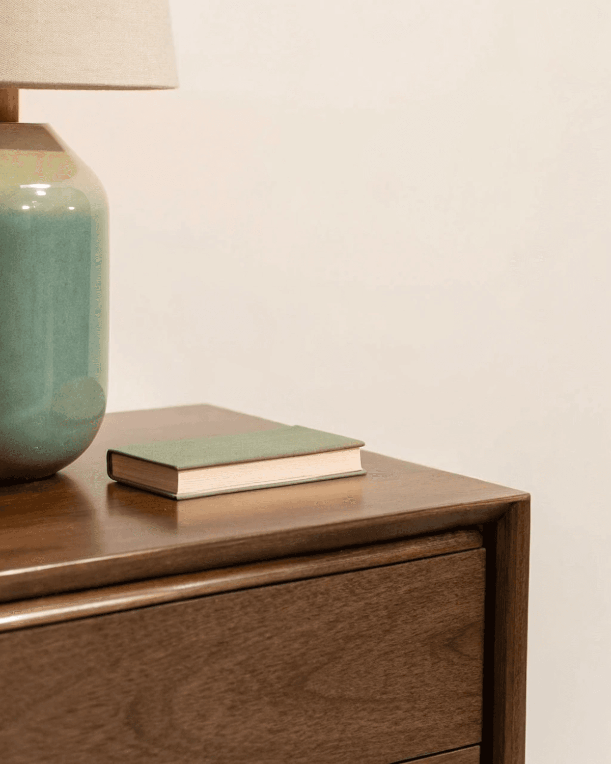 A wooden nightstand with a ceramic table lamp and a small closed book