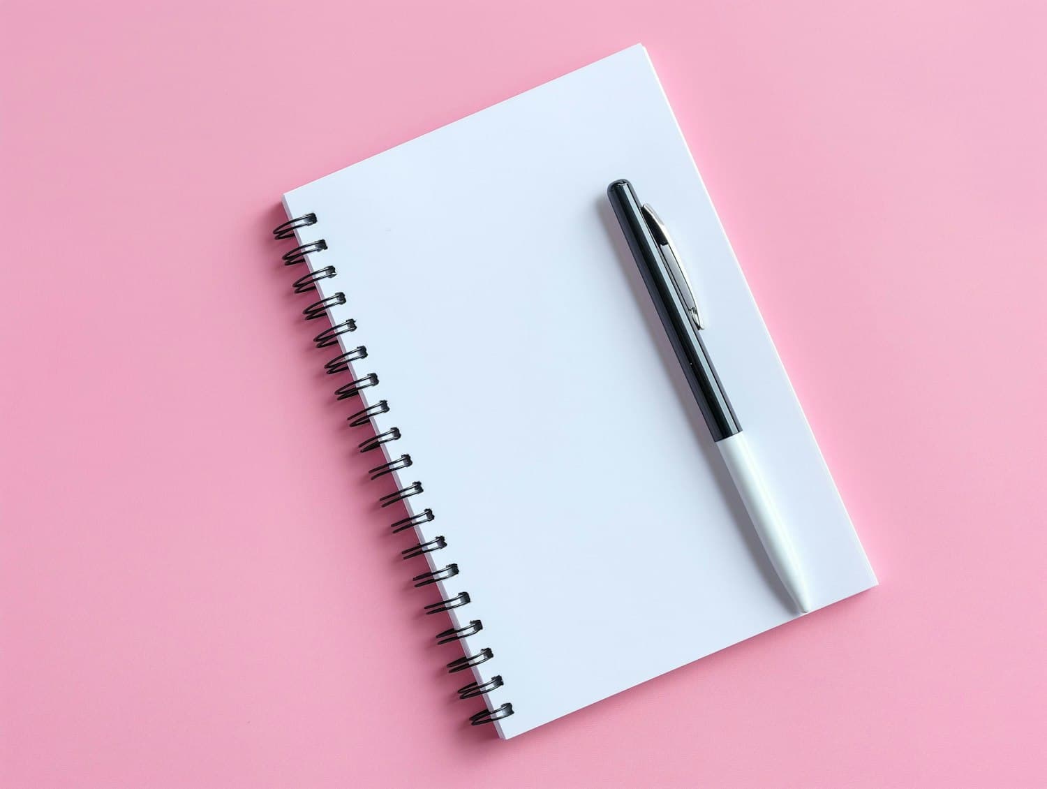 An open spiral notebook with a pen resting on the page